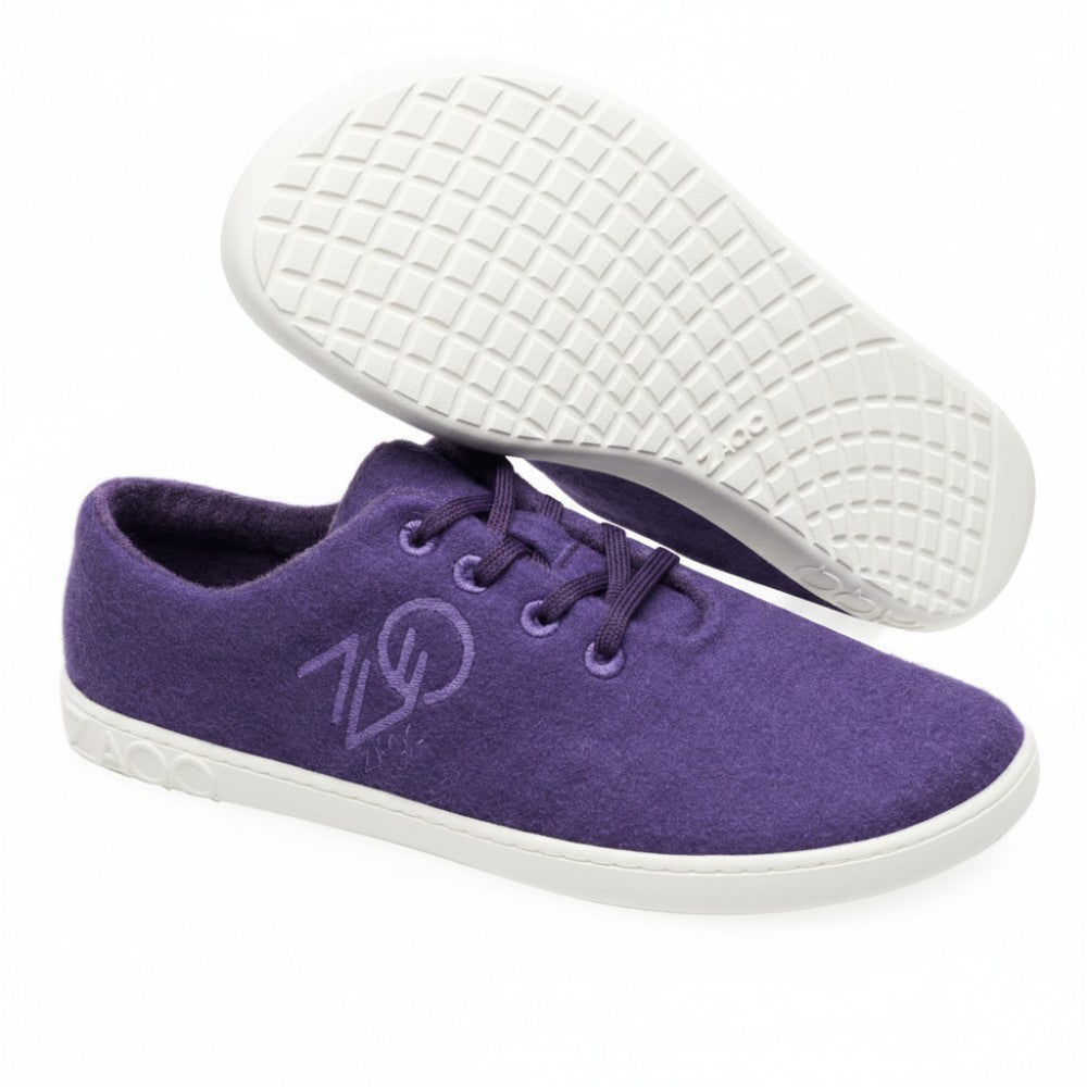Die LIQE Purple Sneaker von ZAQQ bieten eine auffällige wollähnliche Textur. Der rechte Sneaker steht aufrecht und zeigt seine Seite mit dem stilisierten ZAQQ-Logo, während der linke umgedreht ist und die strukturierte Barfußsohle zeigt. Beide Sneaker verfügen über graue Details an der Sohle für einen zusätzlichen Hauch von Stil.