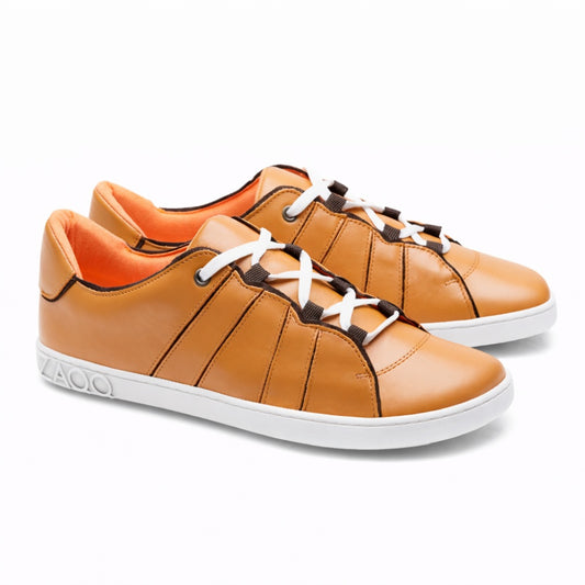 Wir präsentieren den QQQ Low Sierra von ZAQQ: Ein Paar lässige Sneaker aus hellbraunem Nappaleder, komplett mit weißen Schnürsenkeln und flexiblen Kautschuksohlen. Diese Sneaker zeichnen sich durch exquisite braune Nähte und ein leuchtend orangefarbenes Innenfutter aus, die sich alle wunderschön vor einem weißen Hintergrund abheben.