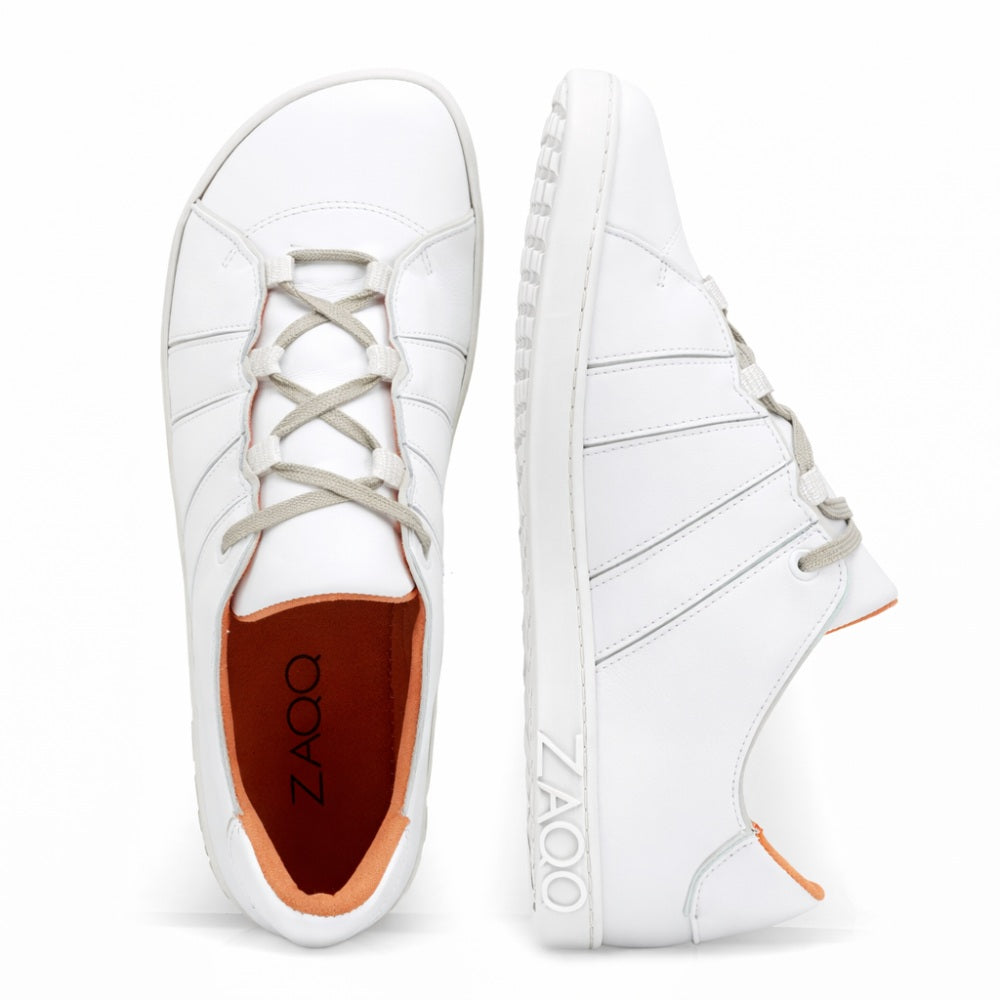 Wir präsentieren den QQQ Low White: Ein Paar weiße Sneaker mit grauen Schnürsenkeln und leuchtend rotem Innenfutter, fachmännisch gefertigt aus atmungsaktivem Premium-Nappaleder. Diese Schuhe sind an der Seite und der Sohle deutlich mit dem ZAQQ-Branding versehen. Vor einem weißen Hintergrund ist ein Schuh von oben zu sehen, während der andere im Seitenprofil gezeigt wird, wodurch das Barfußschuh-Design hervorgehoben wird.