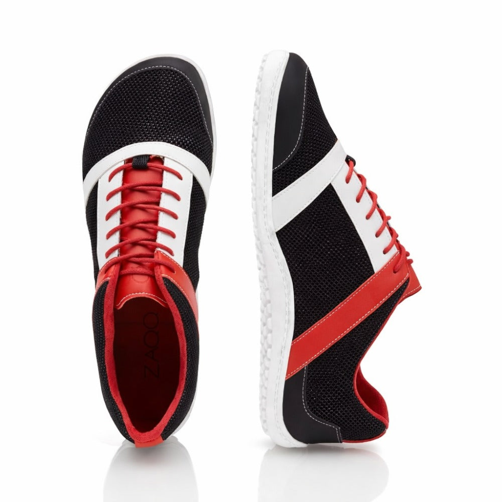Die ZAQQ ZARQA Black Sneaker zeichnen sich durch ein auffälliges Design mit schwarzem Mesh-Gewebe, leuchtend roten Sohlen und Schnürsenkeln sowie markanten weißen Streifen aus. Ein Schuh steht aufrecht, während der andere vertikal steht, um seine Sohle zu präsentieren. Dies ist für jeden Runningschuh-Fan die perfekte Verschmelzung von Stil und Funktionalität.